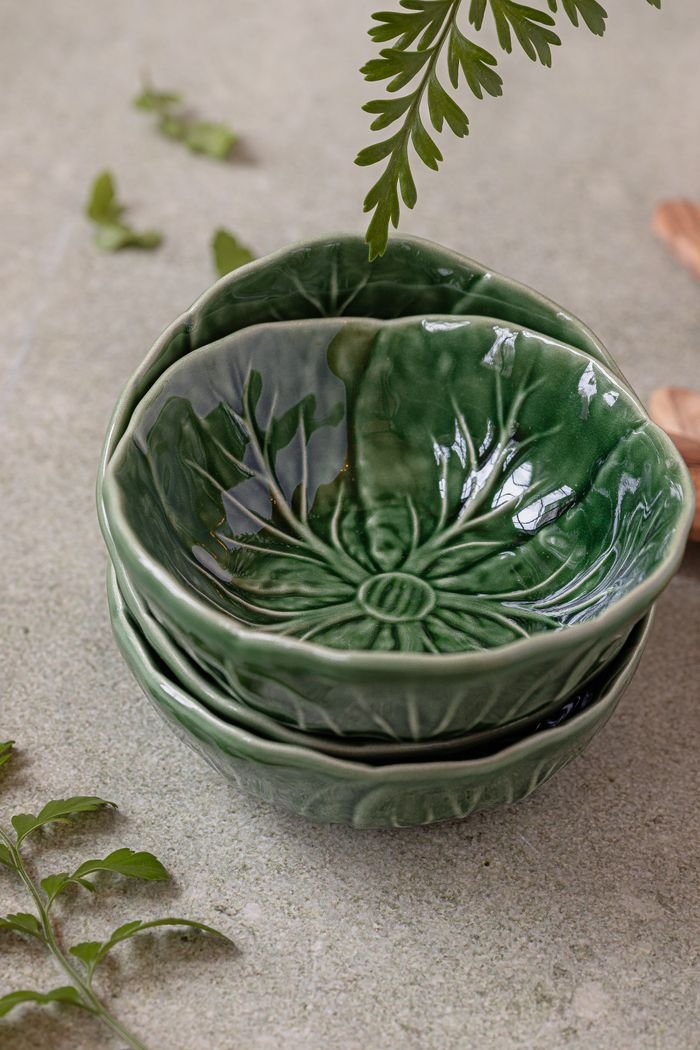 Close-up of stacked green ceramic bowls on a stone surface with decorative leaves.