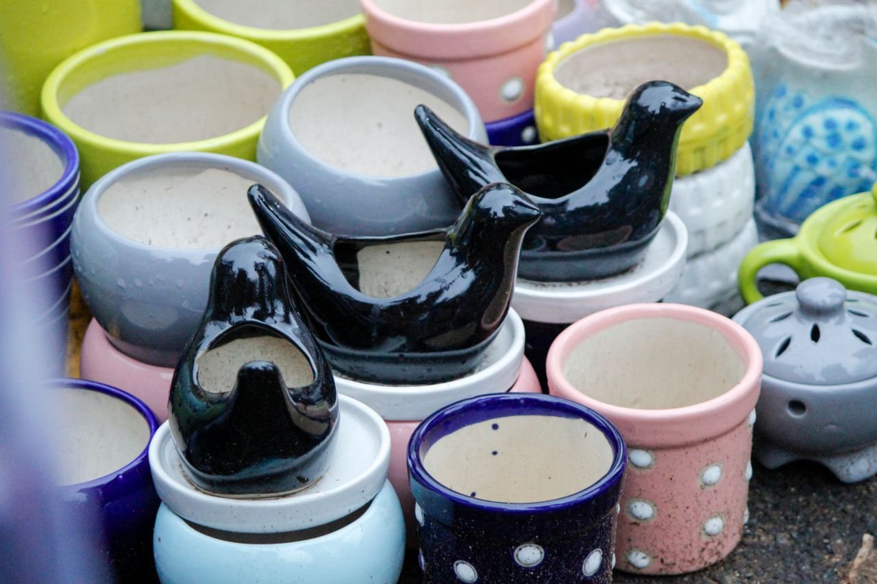 Assorted colorful ceramic pots and decorative bird sculptures on display at a market stall.
