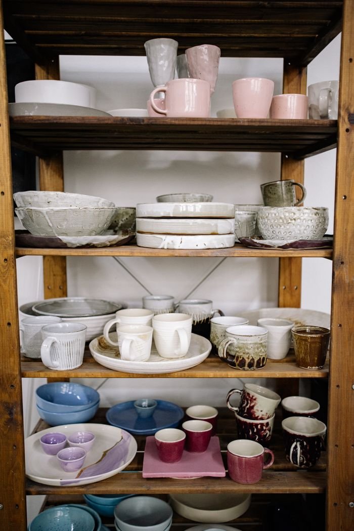 A collection of handcrafted ceramic cups and bowls displayed on wooden shelves.